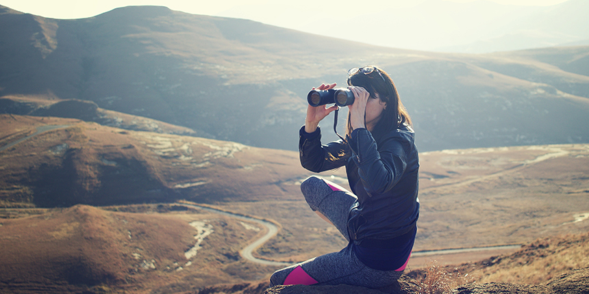 Woman sitting on a mountaintop looking into binoculars