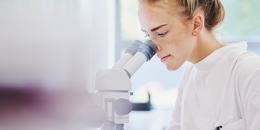 Woman in a lab coat looking into a microscope